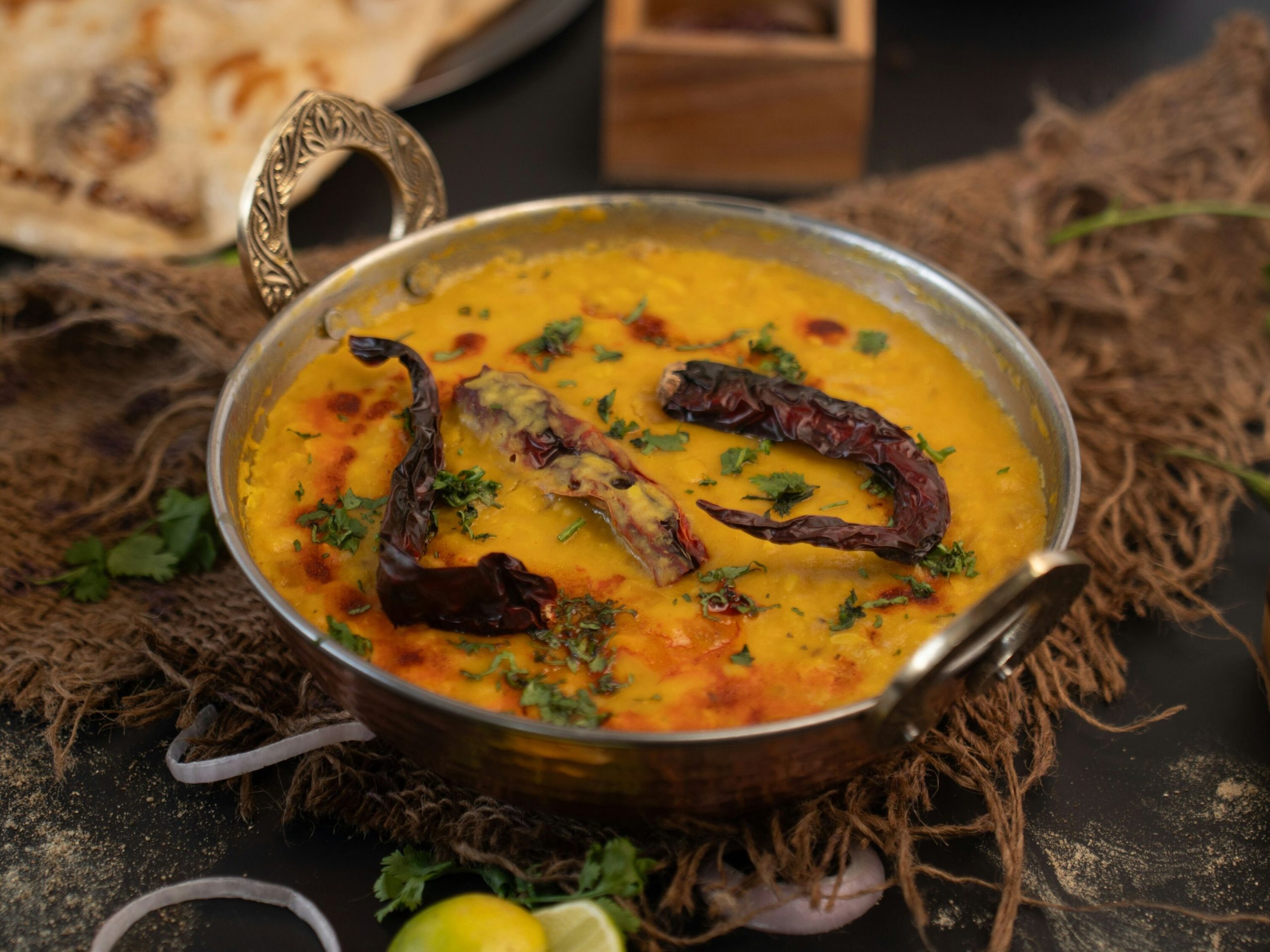 Steaming bowl of dal tadka with sizzling ghee tempering being poured over in a brass serving bowl