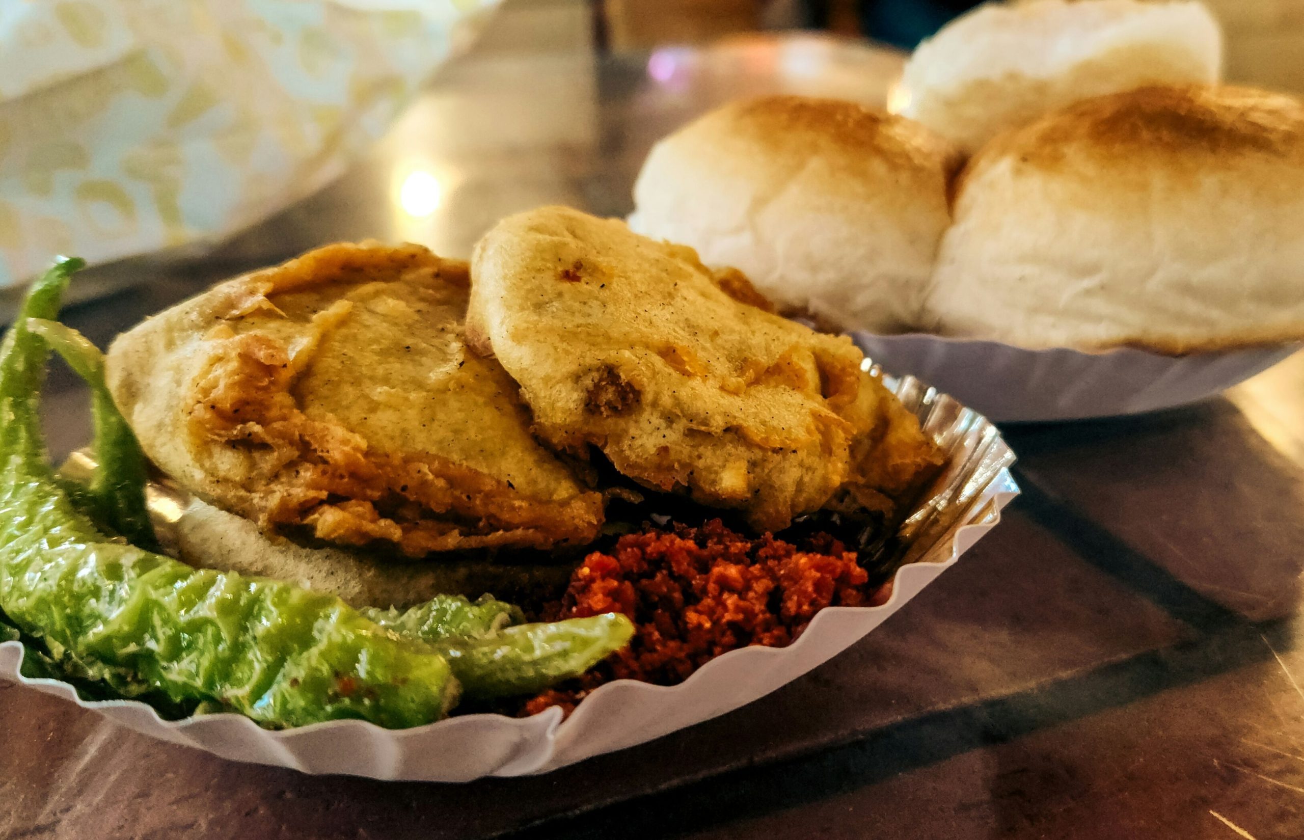 Freshly made vada pav with green chutney and dry garlic chutney on newspaper in Mumbai street style