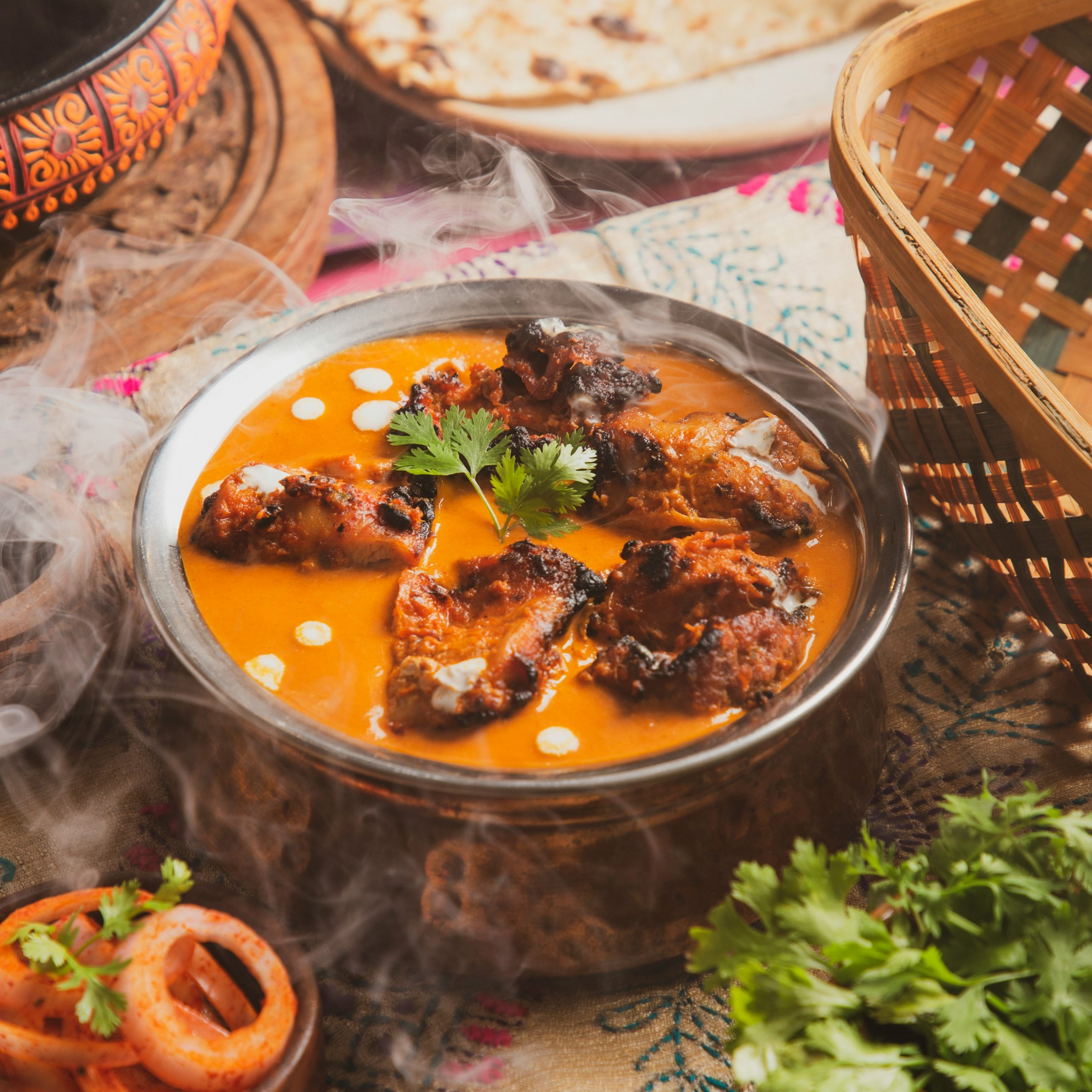 Creamy homestyle butter chicken in a black iron kadai with fresh coriander and naan on a wooden table