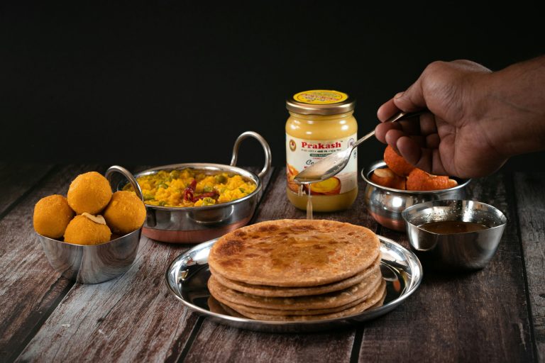 Golden aloo paratha on a steel plate with white butter, green chutney and a glass of lassi on a wooden table